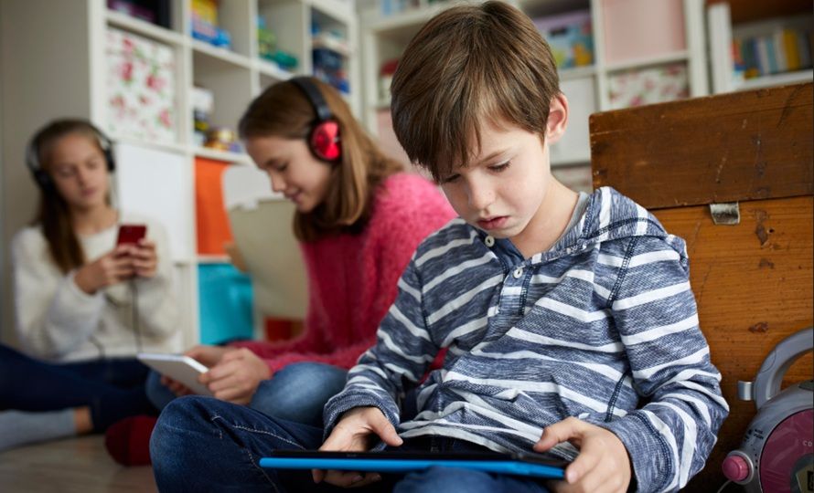 Trois enfants concentrés sur leurs écrans respectifs dans une chambre