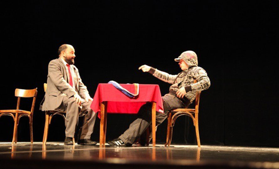 2 hommes assis autour d’une table sur une scène de théâtre