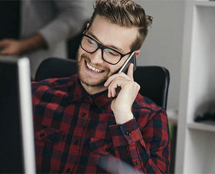 Un homme souriant avec son téléphone portable devant un ordinateur